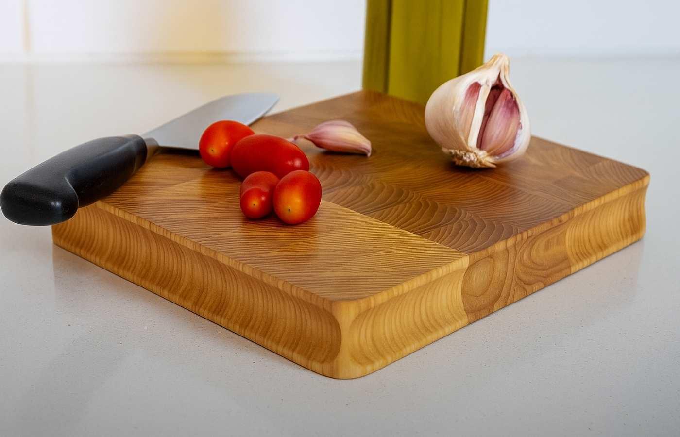 Wooden cutting board with fresh tomatoes, garlic cloves, and a kitchen knife on a white countertop