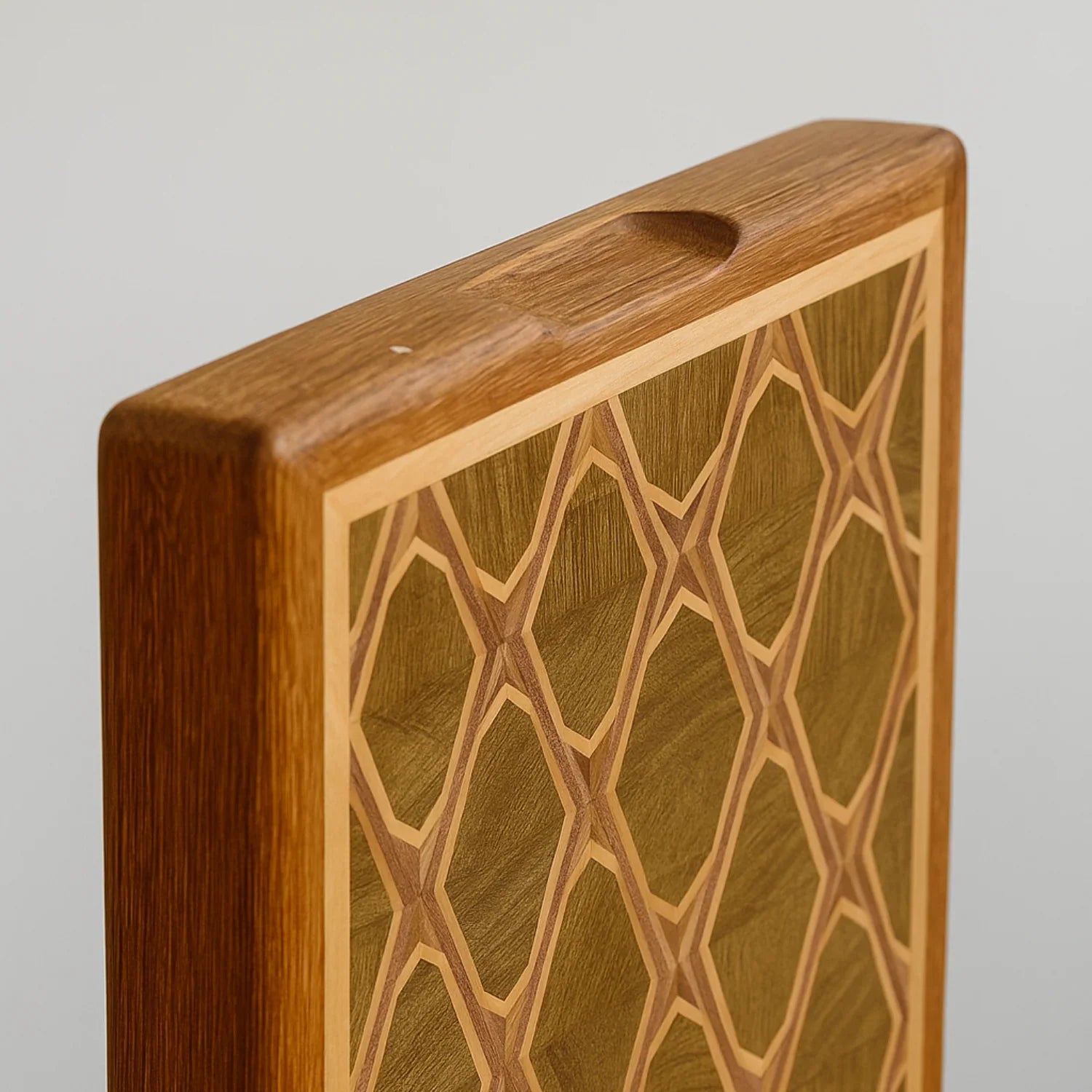 Close-up of a handcrafted wooden Majlis cutting board with geometric inlay pattern and grip handle