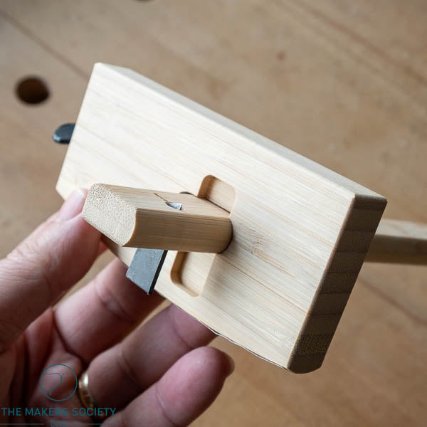 Wooden tool held by a hand on a wooden surface, with 'The Makers Society' branding.