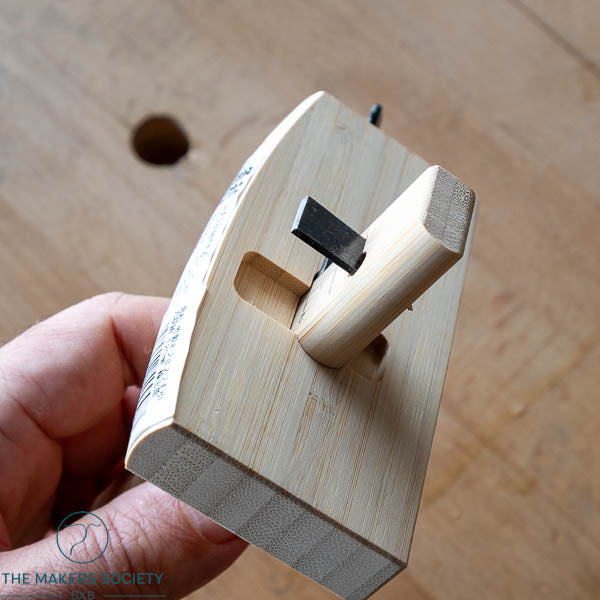 Wooden plane tool held by a hand on a wooden surface.