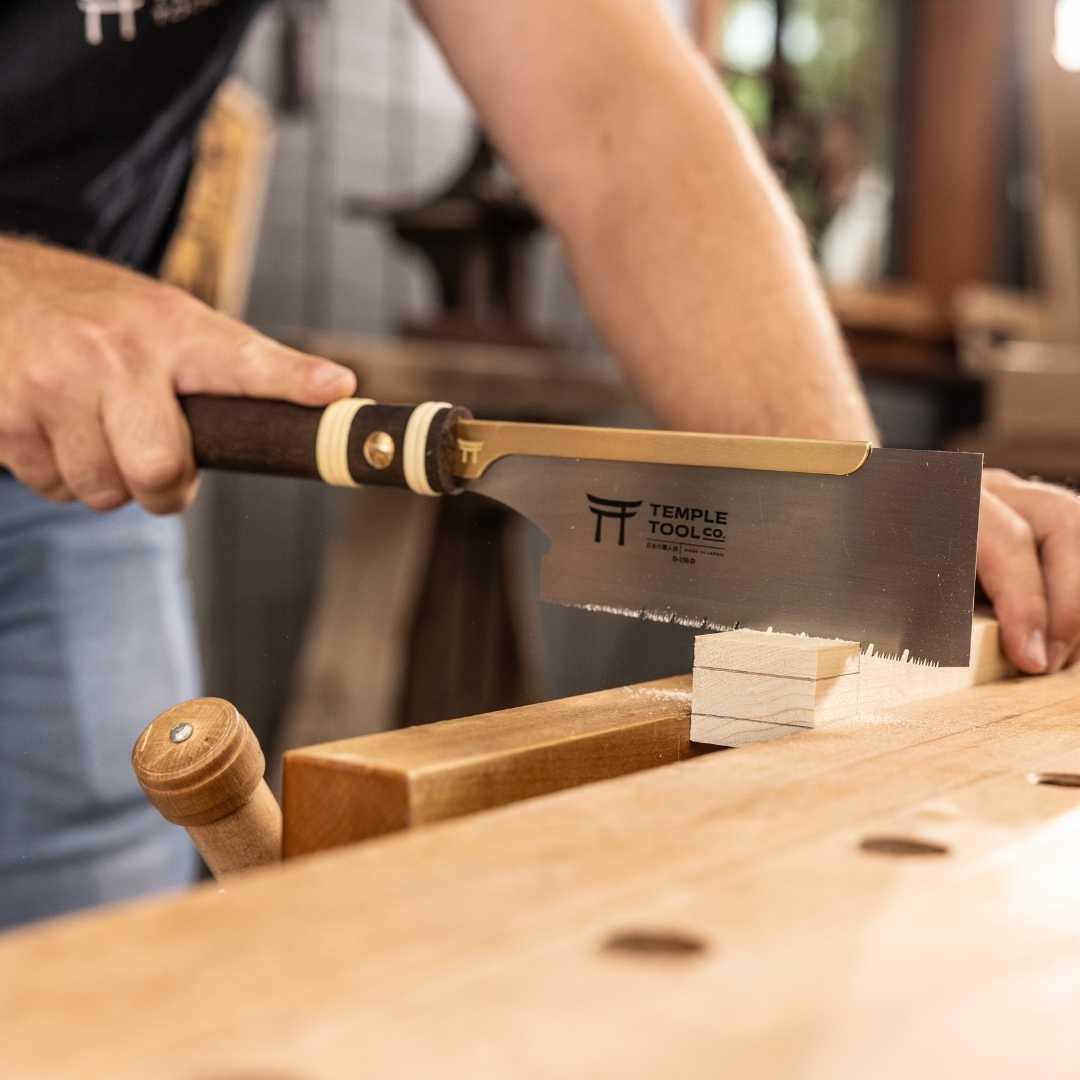 Person using Temple Tool Dozuki pull saw with fine teeth to cut wood on a workbench