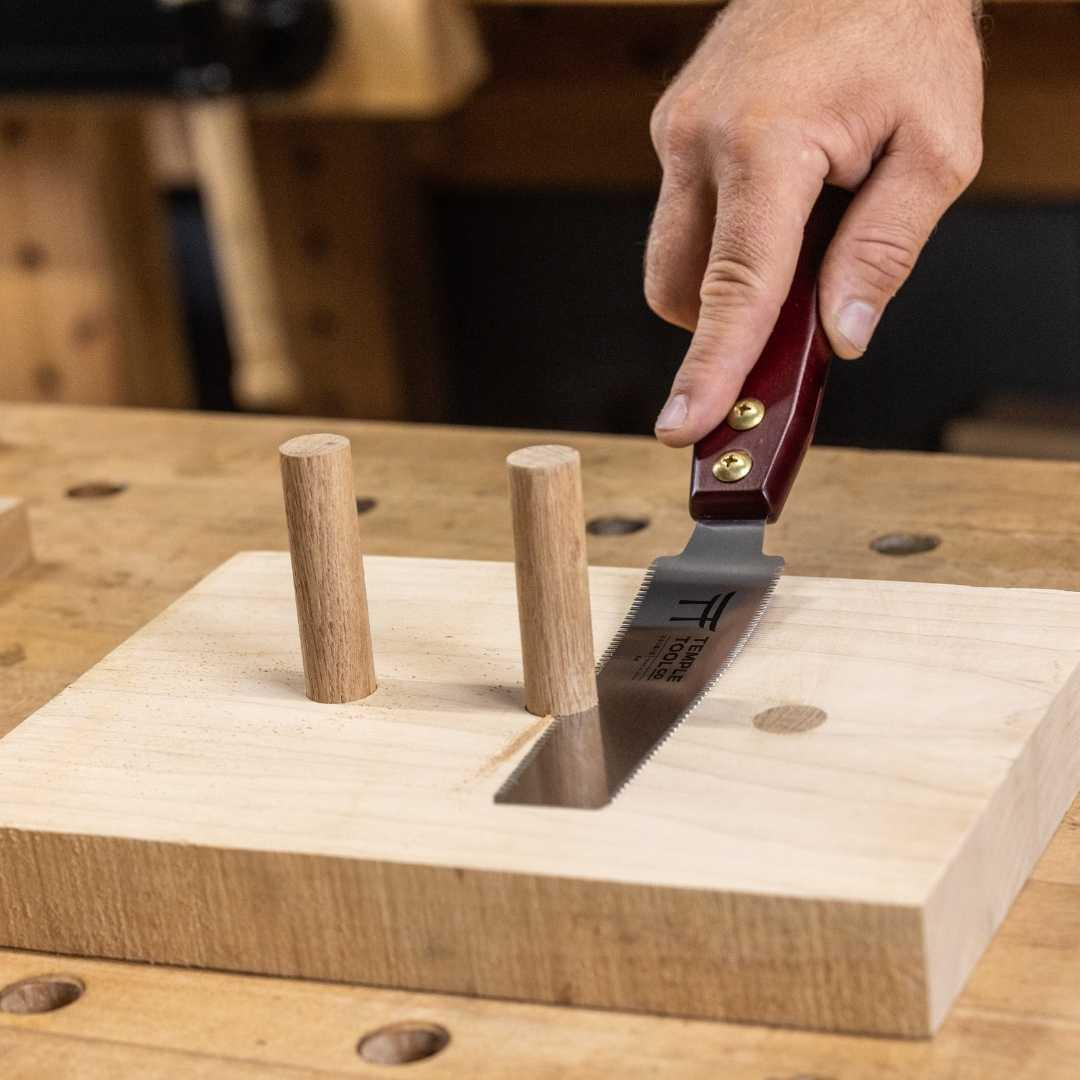 Hand using Temple Tool 150mm flush cut pull saw cutting wooden dowels on workbench