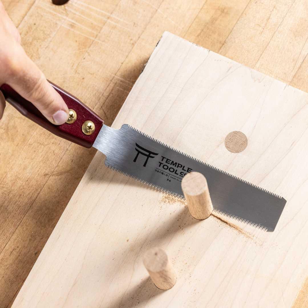 Hand using Temple Tools 150mm flush cut pull saw to trim wooden dowel on light wood board