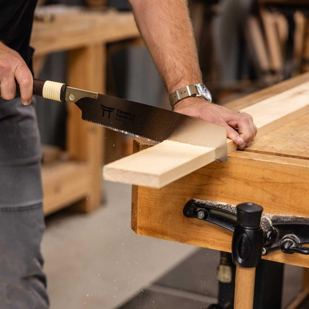 Person using Temple Tool Kataba pull saw to cut a wooden plank on a workbench in a workshop