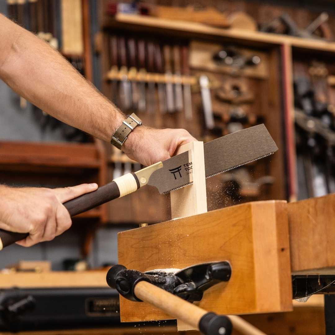 Man using Temple Tool Kataba pull saw to cut wood on a woodworking bench in a workshop